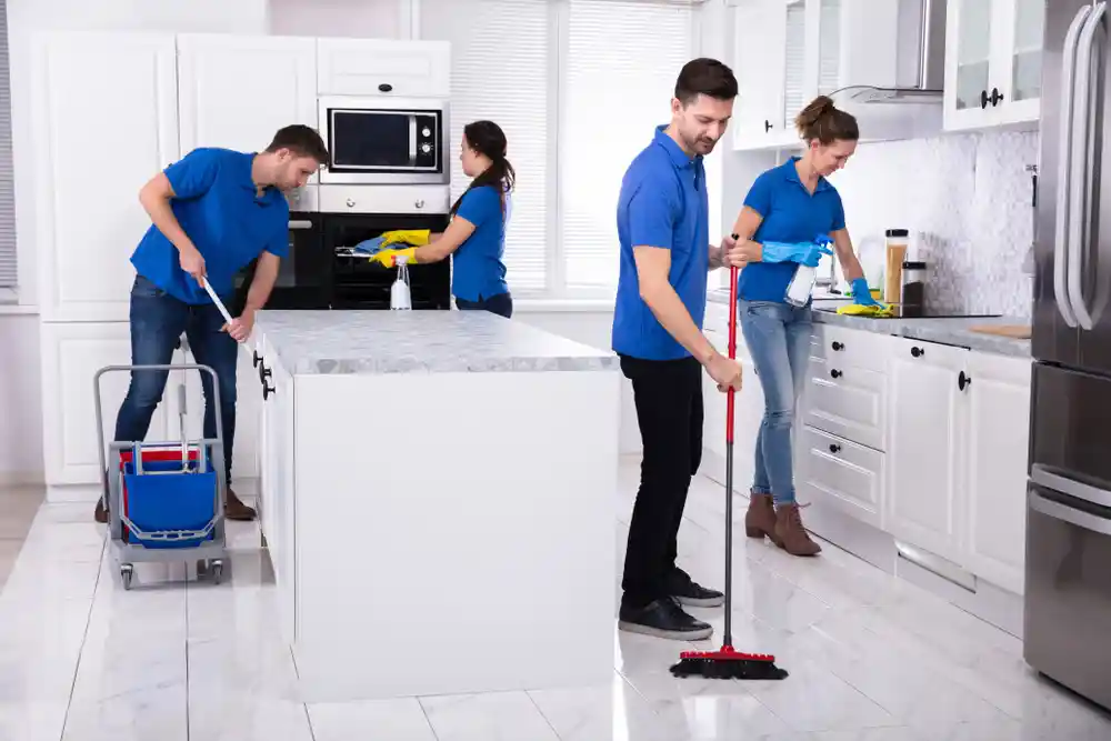 Cleaning staff in blue uniforms sanitizing a modern kitchen.